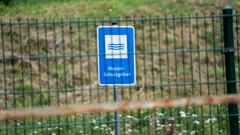 Blaues Schild mit der Aufschrift "Wasserschutzgebiet" steht hinter einem Zaun. 